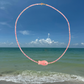 Necklace with pink fish pendant over a beach and ocean scene