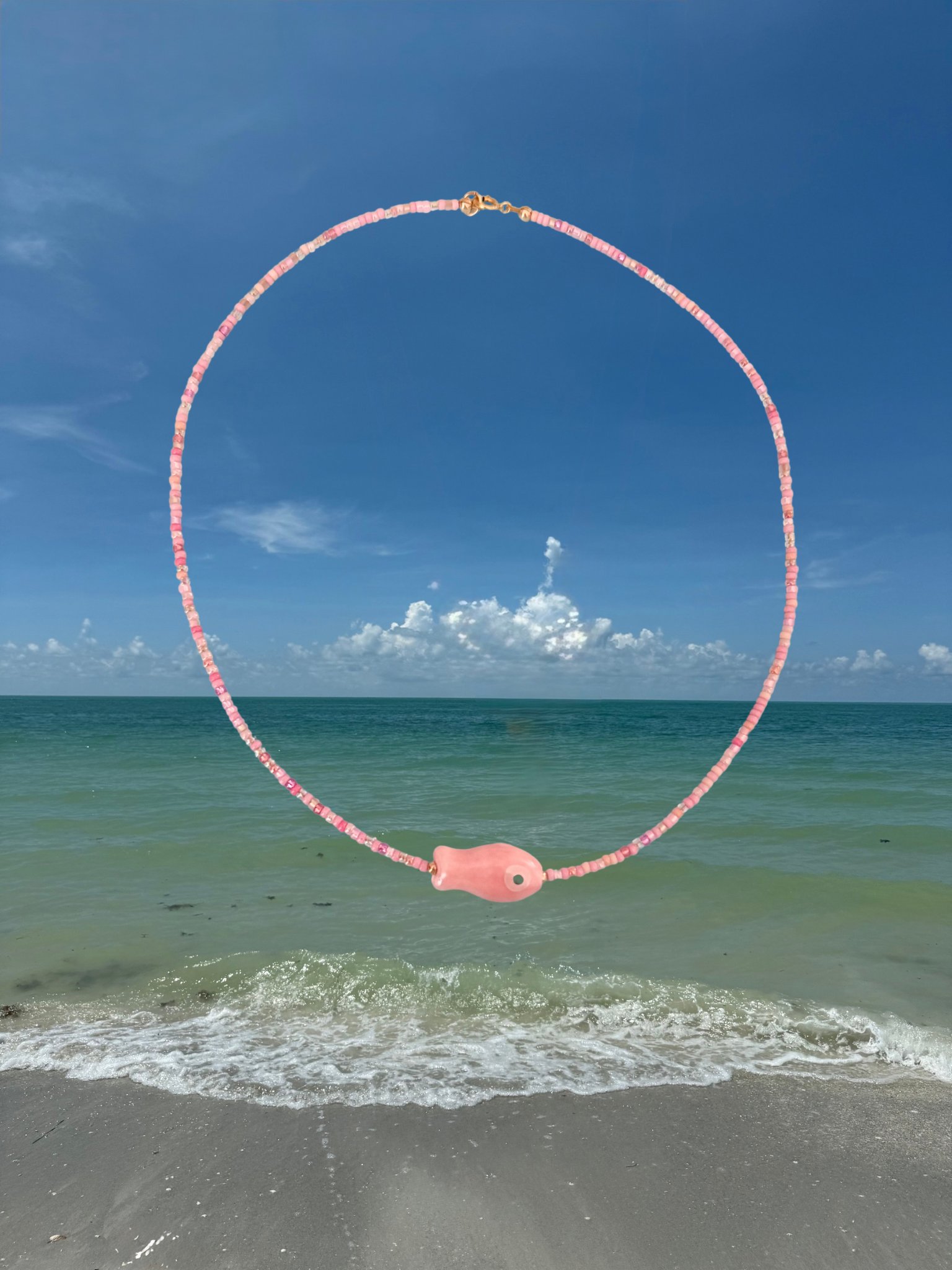 Necklace with pink fish pendant over a beach and ocean scene